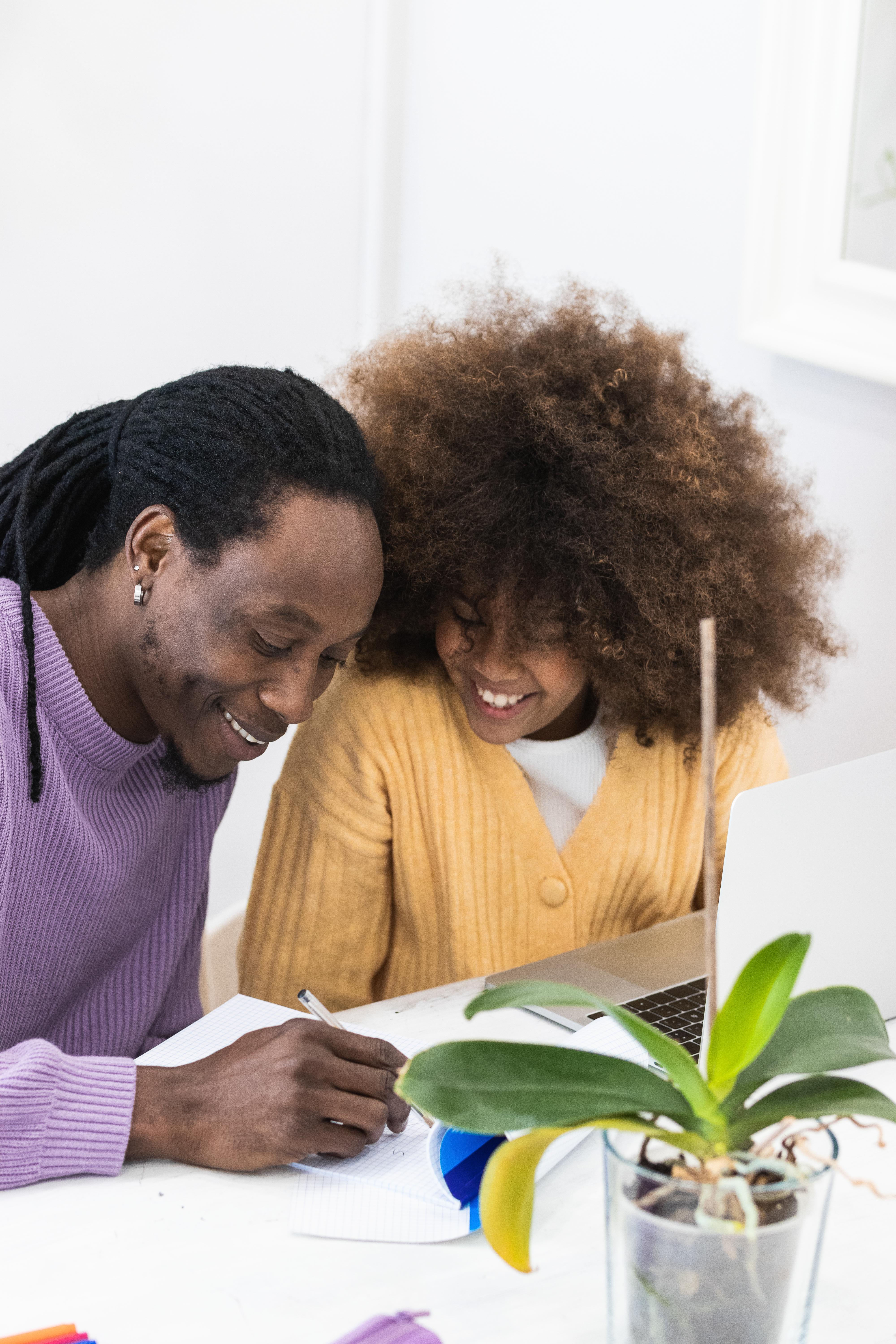 An adult and child smile together while doing homework
